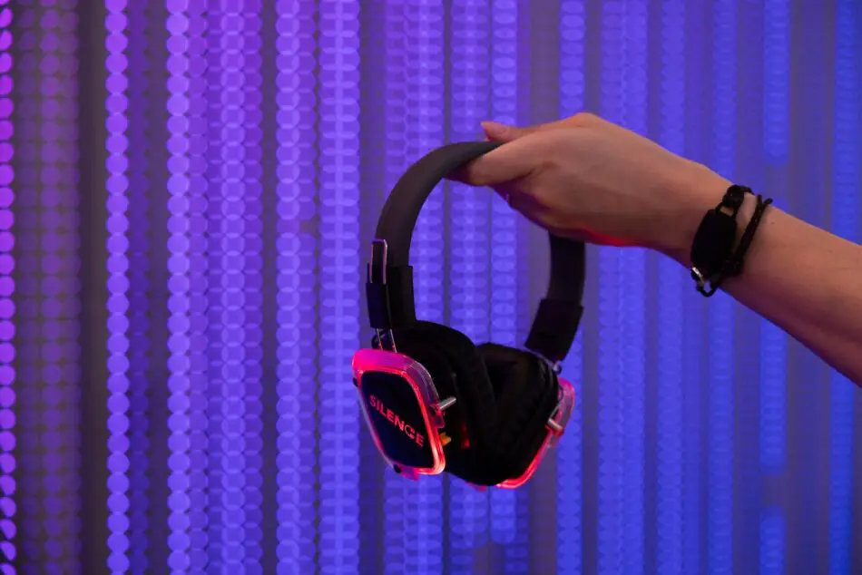 Hand holds neon pink over-ear headphones against a purple LED backdrop