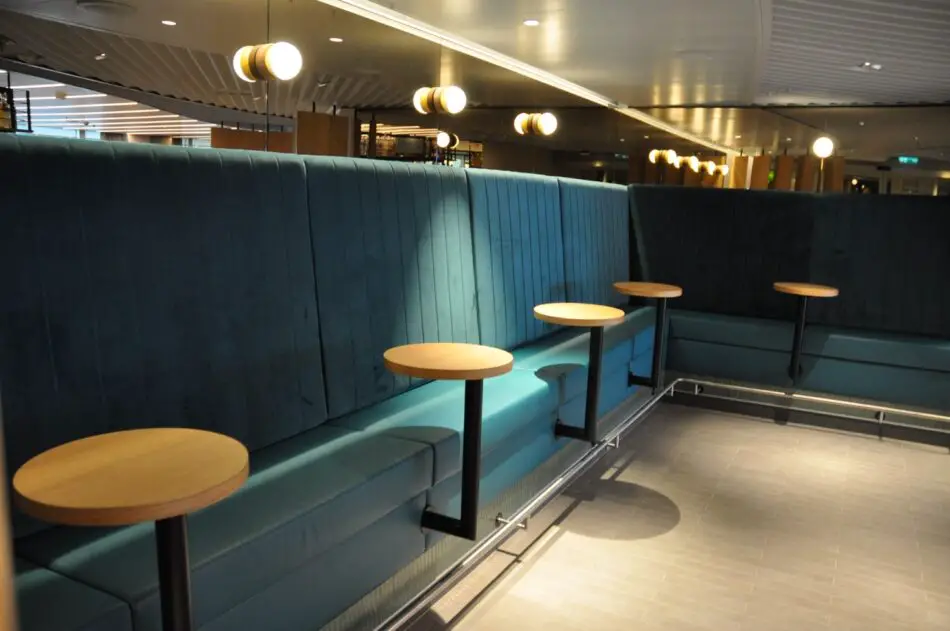 Teal upholstered booth seating with round wooden tables on a Virgin Voyages cruise ship lounge