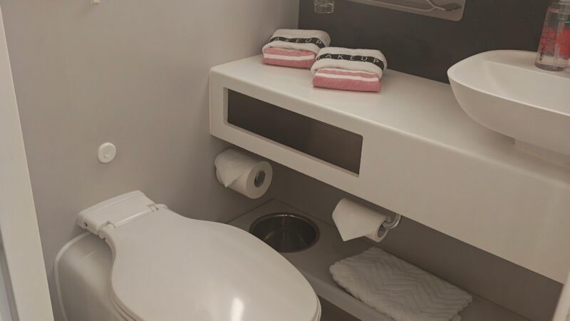 Bathroom of a Virgin Voyages cruise ship cabin, featuring a toilet, sink, and towels.