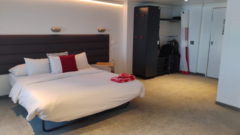 Spacious Virgin Voyages cruise ship cabin with a modern bed, ambient lighting, and an open wardrobe area.