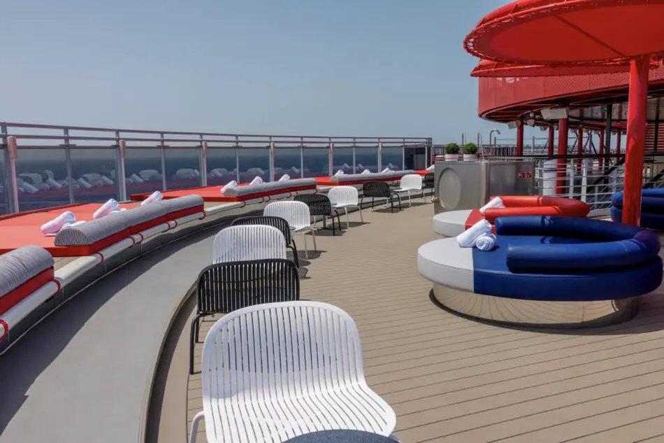 Sunlit Virgin Voyages cruise ship deck with circular red and blue lounge seats