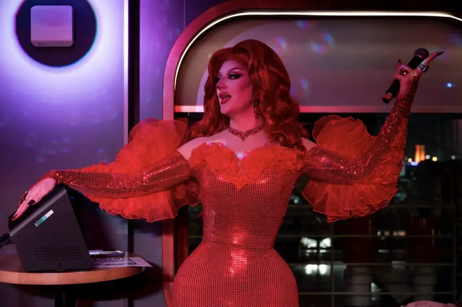 Drag queen in a red sequined gown performing with a microphone on a Virgin Voyages cruise ship