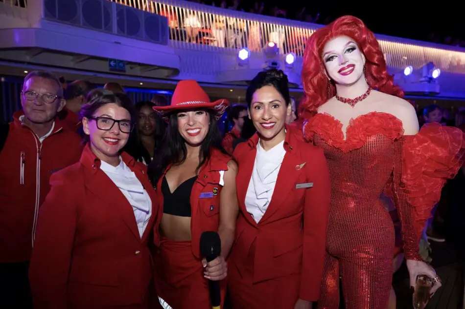 Group of Virgin Voyages crew in red uniforms with a red-clad drag performer on a cruise ship