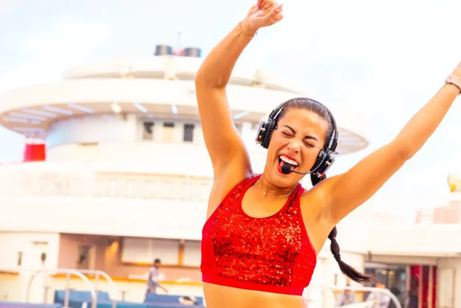Smiling woman in a red sequined top wearing a headset on Virgin Voyages cruise ship deck