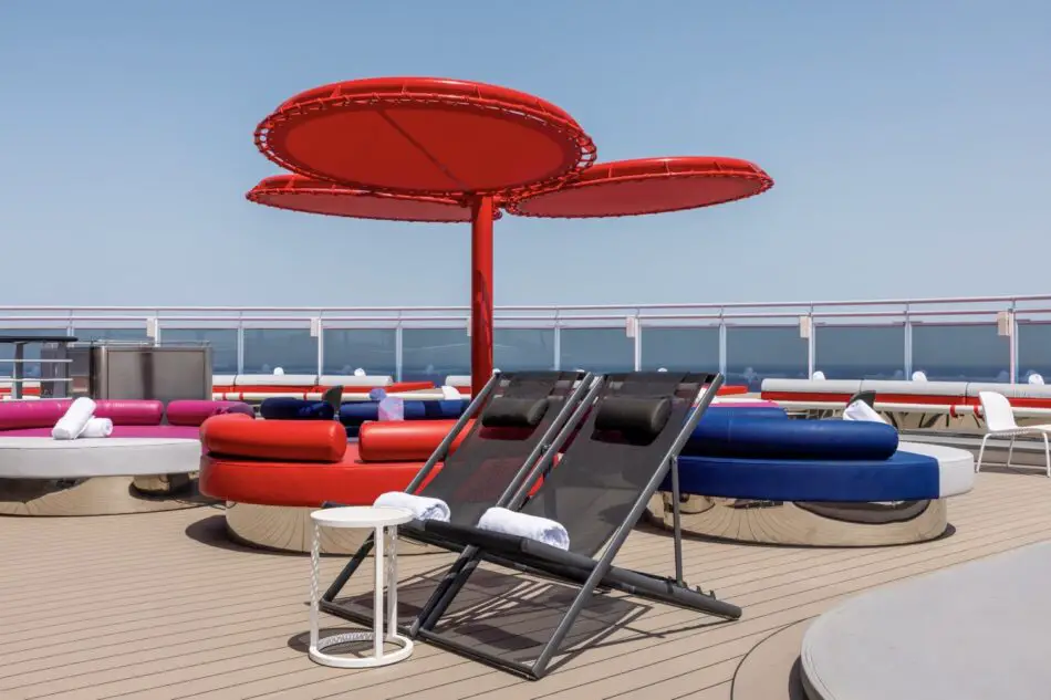 Red circular shade canopies over lounge chairs on a Virgin Voyages cruise ship deck
