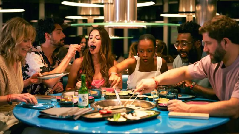 Group of friends dining around a blue circular table with a built-in grill on a Virgin Voyages cruise ship at Gunbae