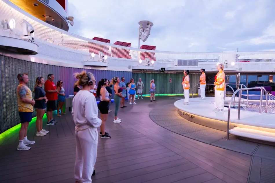 Audience wearing wireless headphones on a Virgin Voyages cruise ship deck watches a stage show