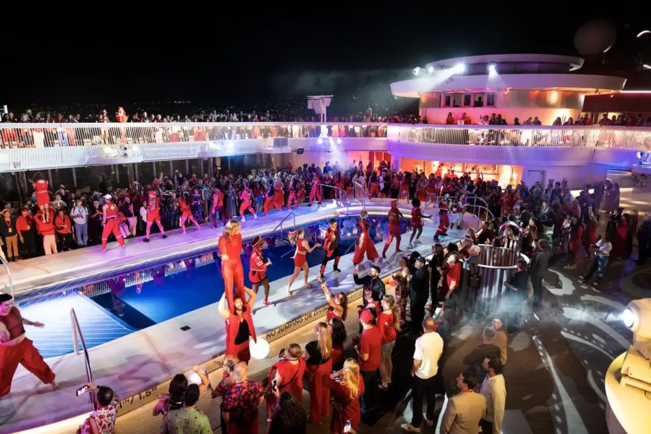 Crowd dressed in red around a pool during a nighttime event aboard a Virgin Voyages cruise ship