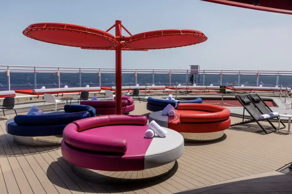 Colorful circular lounge seats around a red umbrella on a Virgin Voyages deck