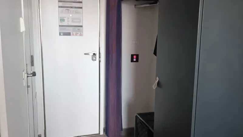 Virgin Voyages cruise ship cabin hallway with entrance door, open wardrobe, and floor storage baskets.