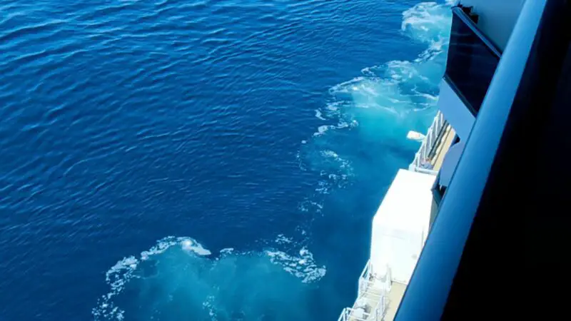 View from a Virgin Voyages cruise ship balcony, overlooking the open ocean and the ship's lower deck with lifeboats.