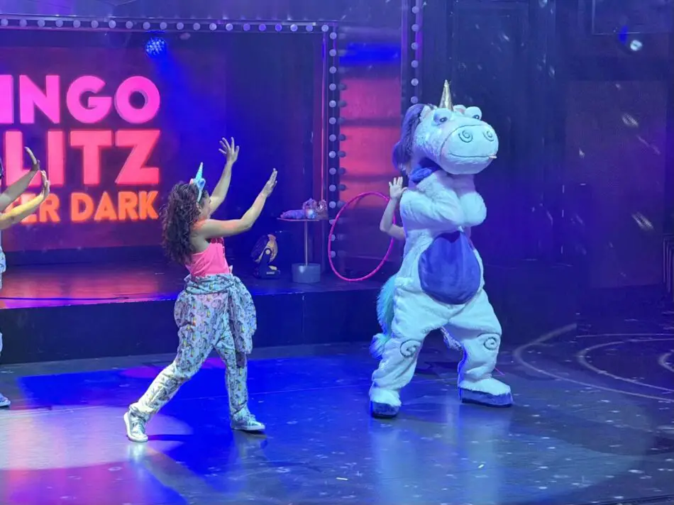 Young girl dances with a unicorn mascot on stage