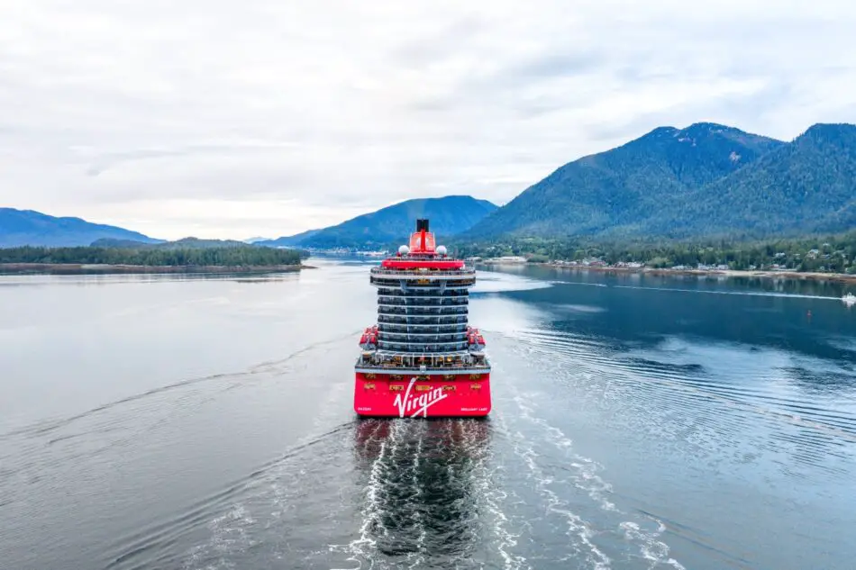 Virgin Voyages cruise ship sailing through a fjord with surrounding mountains