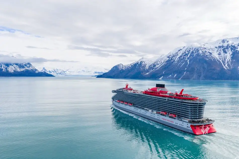 Virgin Voyages cruise ship sailing through an icy fjord with snow-capped mountains