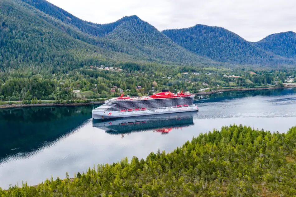 Virgin Voyages cruise ship sails through a forested fjord