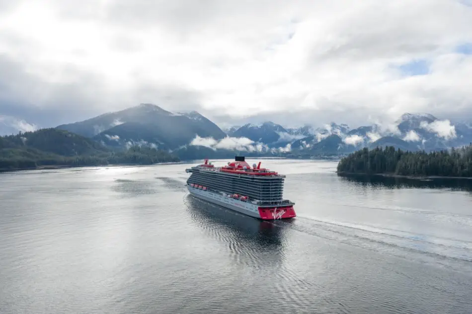 Virgin Voyages cruise ship sailing through a misty fjord with mountains