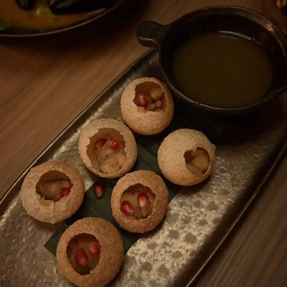 Small hollow pastries filled with cream and pomegranate seeds, served with dark dipping sauce on a metal tray