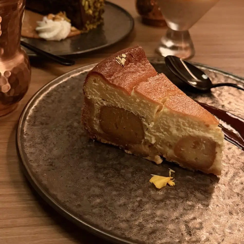 Pear-filled cheesecake slice on a metallic plate, dusted with sugar, with a spoon nearby