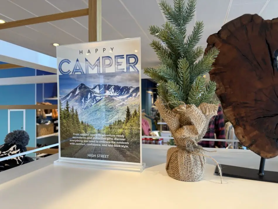 Indoor display featuring a Happy Camper poster showing mountains and a burlap-wrapped pine tree