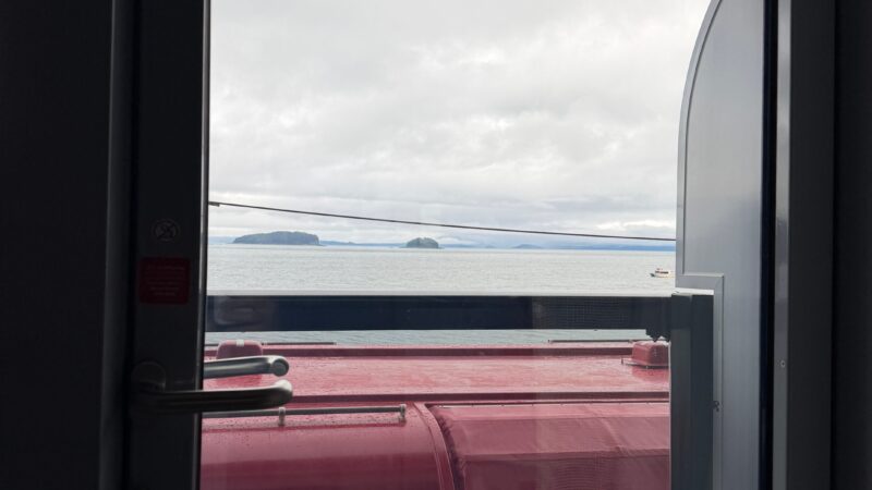 View from a Virgin Voyages cruise ship cabin showing a balcony and the ocean, with a red lifeboat visible outside.