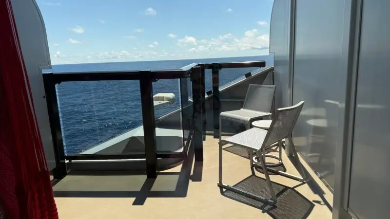 Balcony of a Virgin Voyages cruise ship cabin featuring two chairs, a table, and a hammock with an ocean view.