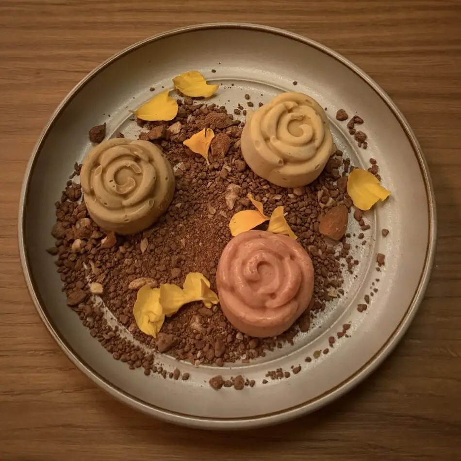 Three swirled mousse desserts on a cocoa crumb bed with yellow petals on a plate