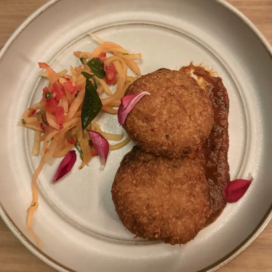 Two breaded croquettes with tomato sauce and a side of shredded vegetables