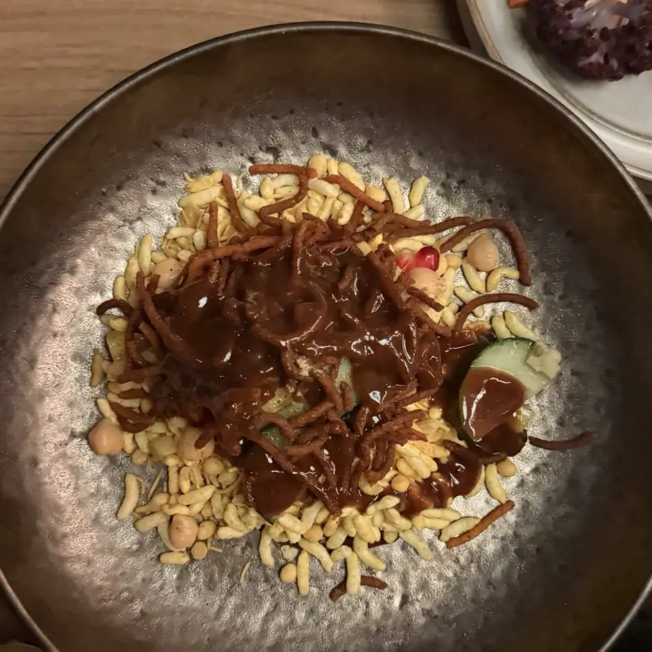 Pan with crispy strands topped with brown sauce, peanuts, and cucumber slices