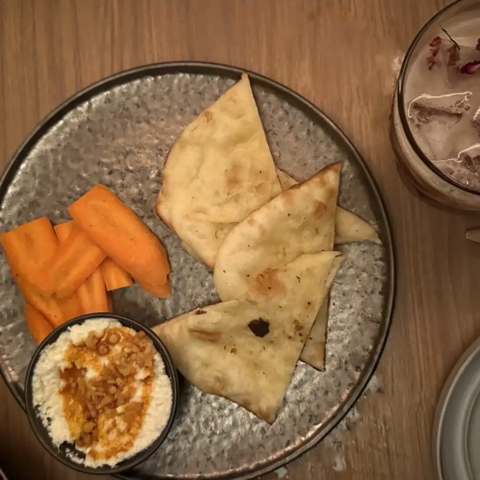 Pita triangles and carrot sticks with dip on a metal plate in a cabin on a Virgin Voyages cruise ship