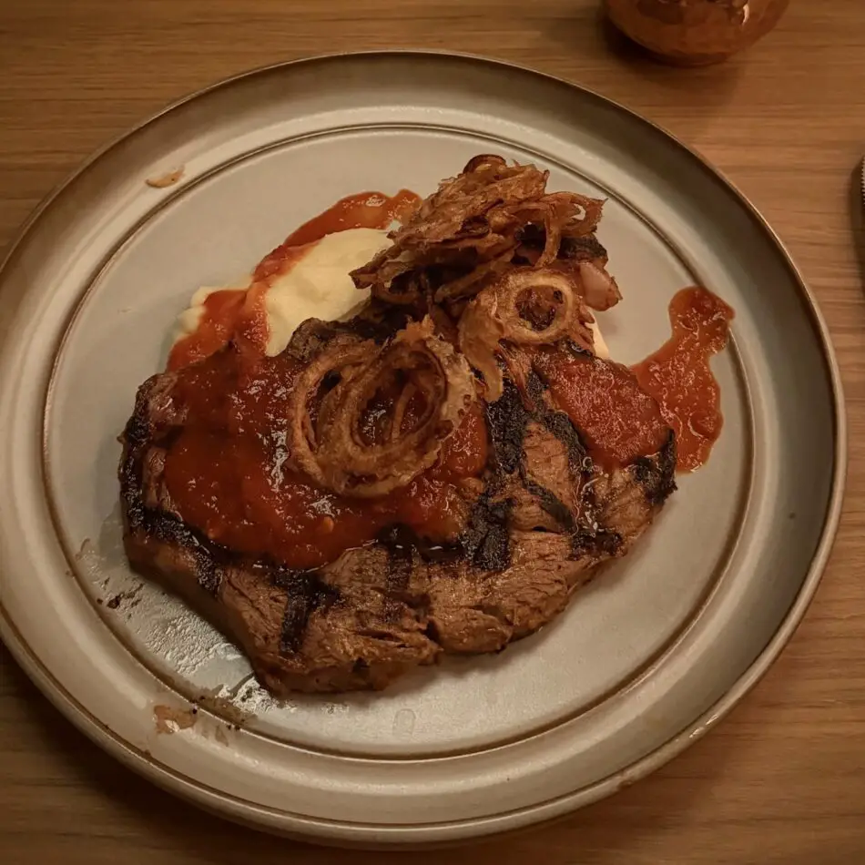 Grilled steak with crispy onion rings and tomato sauce on plate