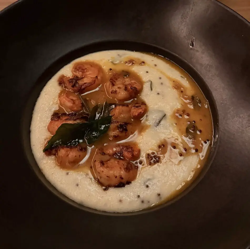 Shrimp in a creamy white sauce with curry leaves and mustard seeds in a black bowl