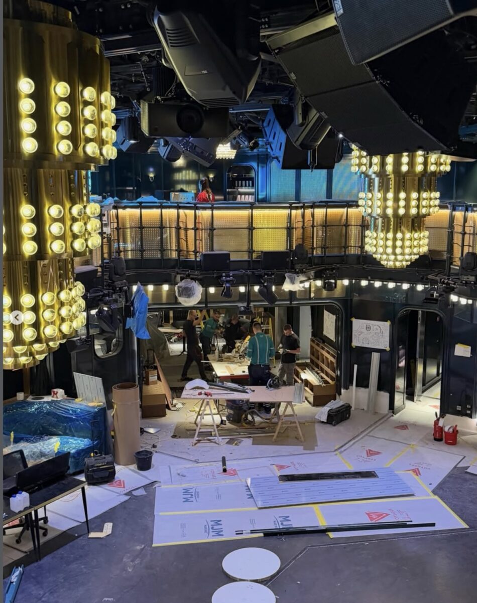 Backstage area of a shipboard theater under construction with large lighting rigs and crew at work