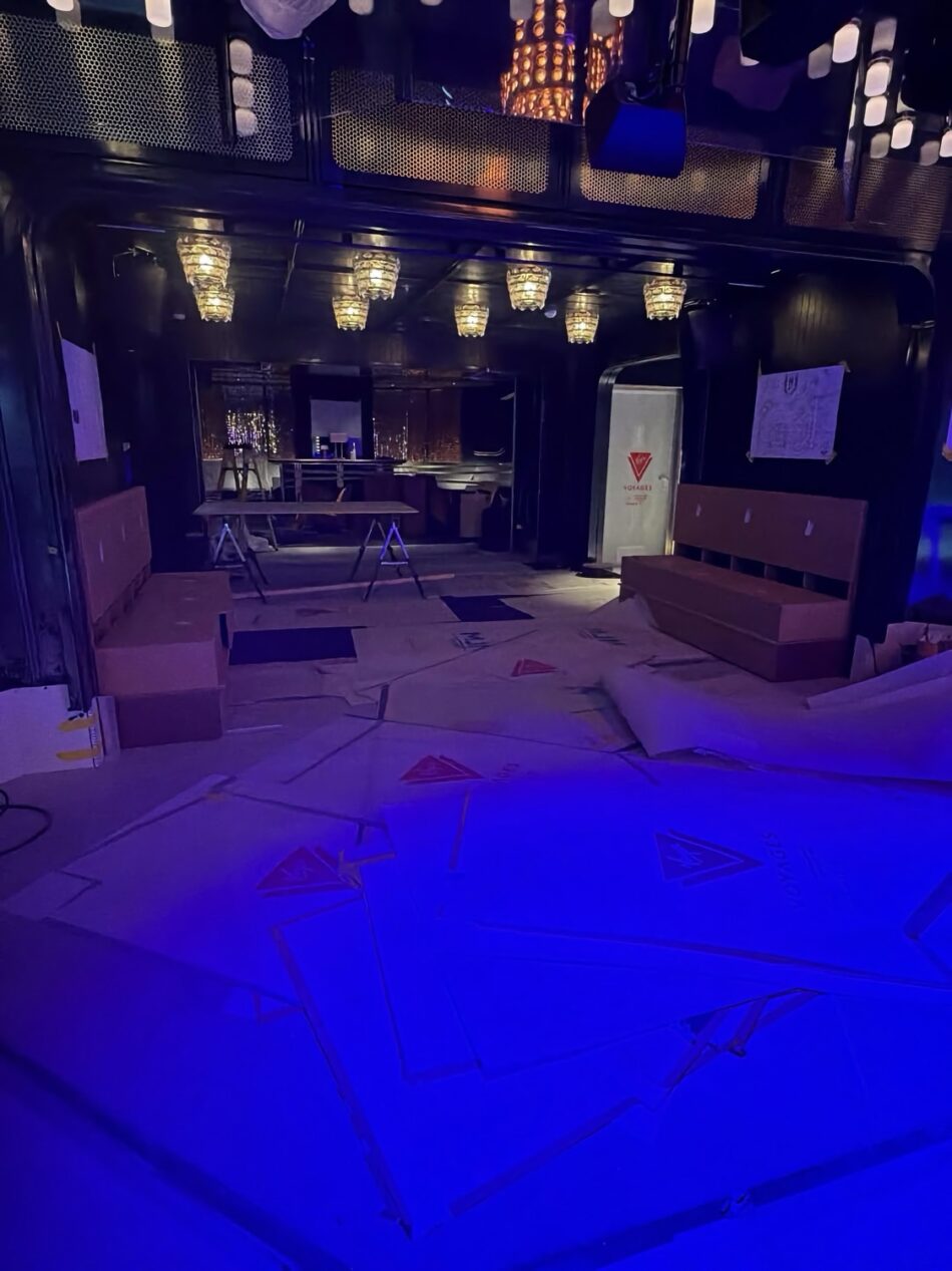 Dim blue-lit club interior with chandeliers and scattered packing materials