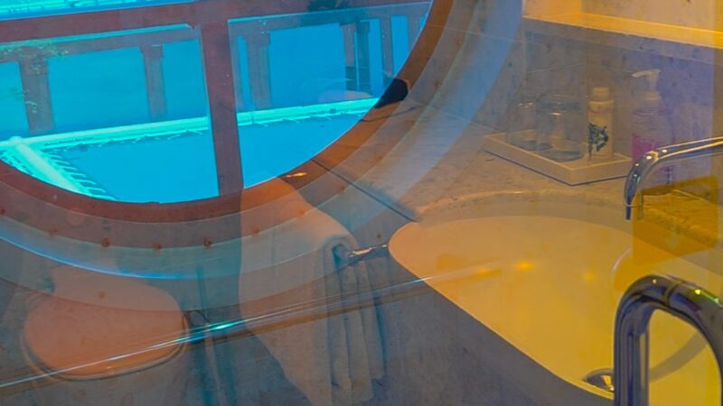Virgin Voyages cruise ship cabin bathroom with a round porthole window showing an ocean view.