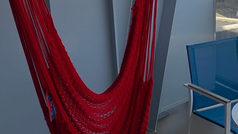 Red hammock on a Virgin Voyages cruise ship balcony, with a blue chair and a small table nearby.
