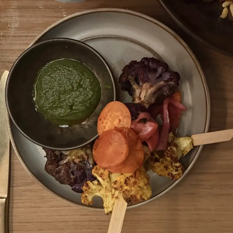 Plate with green sauce in a bowl and assorted roasted vegetables and skewers