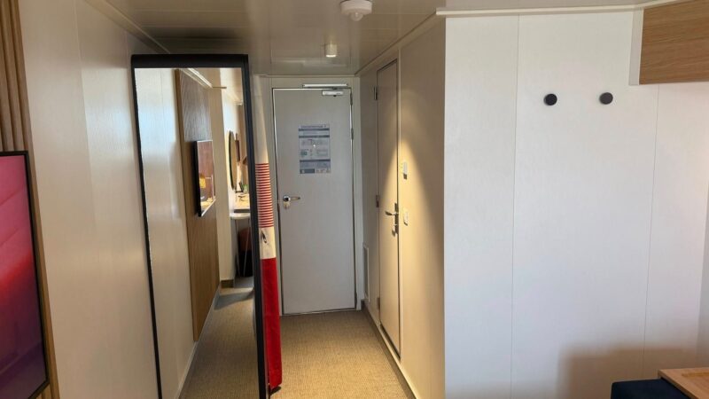 Virgin Voyages cruise ship cabin interior featuring a hallway with a full-length mirror and visible door.