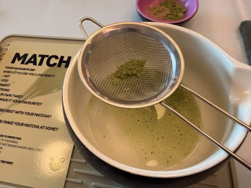 Matcha tea preparation with a metal mesh sieve over a bowl