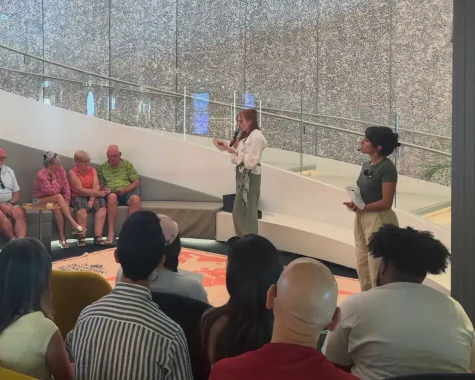 Two hosts address an audience in a cruise ship atrium
