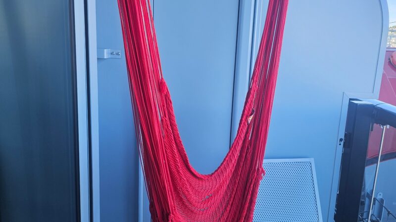 Red hammock on a Virgin Voyages cruise ship balcony with a white chair.