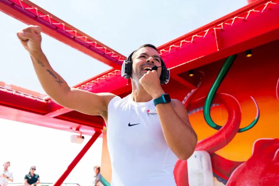 Male crew member with headset gesturing on a bright red cruise ship deck