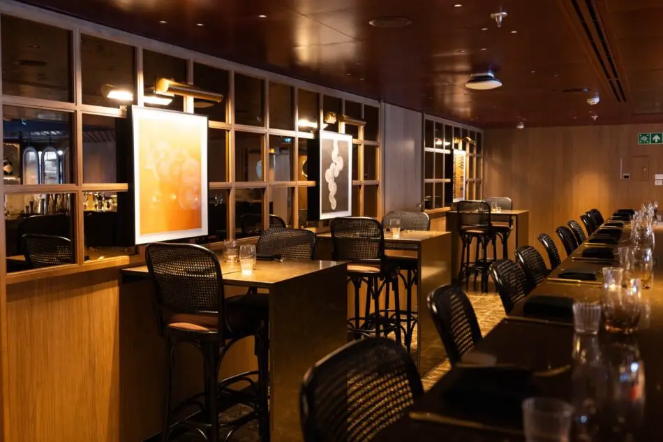 Dimly lit cruise ship dining area with wood paneling and bar stools