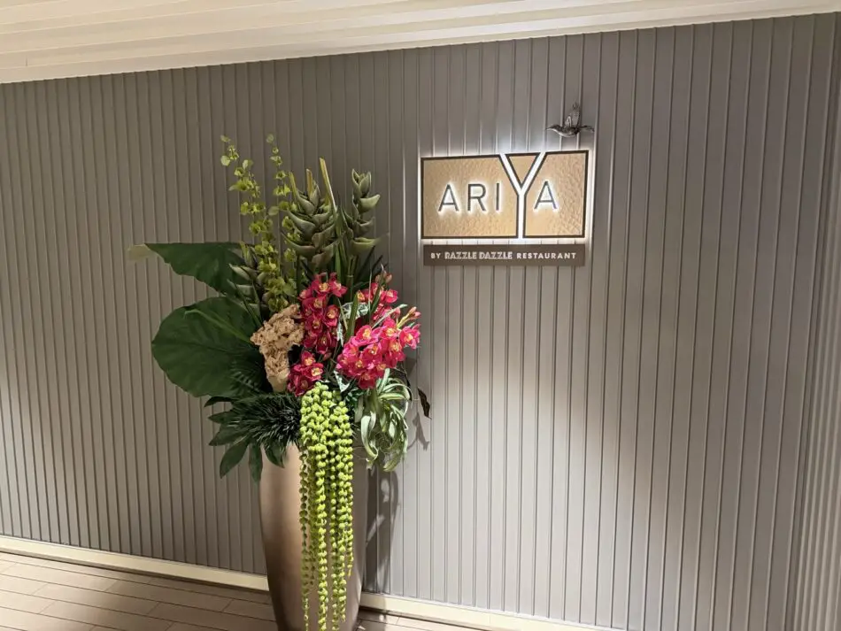 Ariya sign for Razzle Dazzle Restaurant on a Virgin Voyages cruise ship lobby with a tall floral arrangement