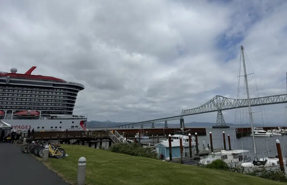 Virgin Voyages cruise ship docked at a harbor with a tall suspension bridge in the background