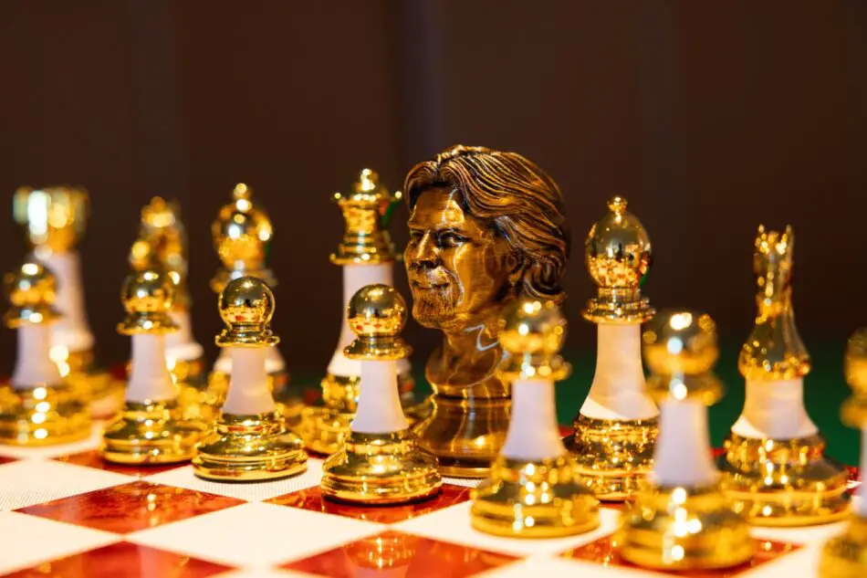 Close-up of a gold chess set with a carved bust centerpiece on a red and white checkered board