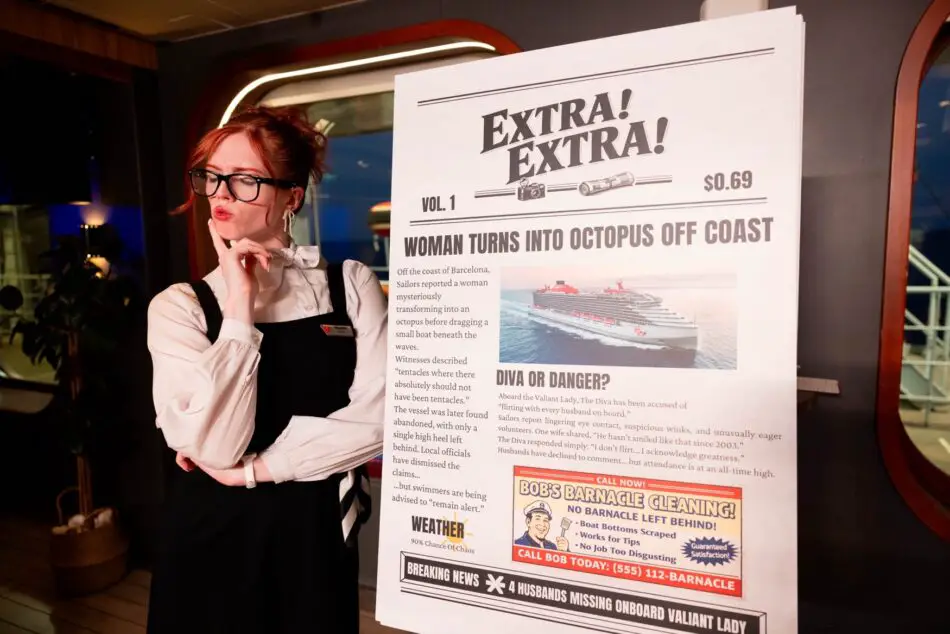 Crew member wearing glasses beside a large newspaper prop aboard a Virgin Voyages cruise ship