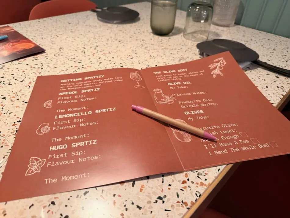 Open olive oil tasting menu on a speckled countertop with a pencil