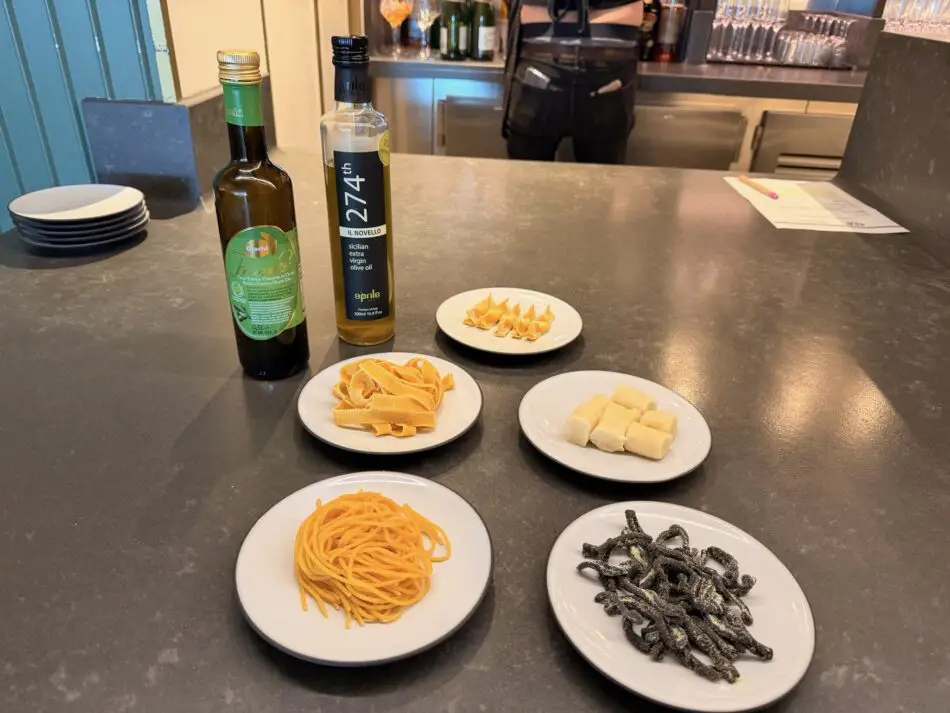 Assorted plates of colored pasta on a bar counter with olive oil bottles and a bartender in the background