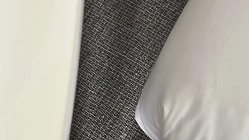 View of a Virgin Voyages cruise ship cabin with a bed and gray patterned carpet below.