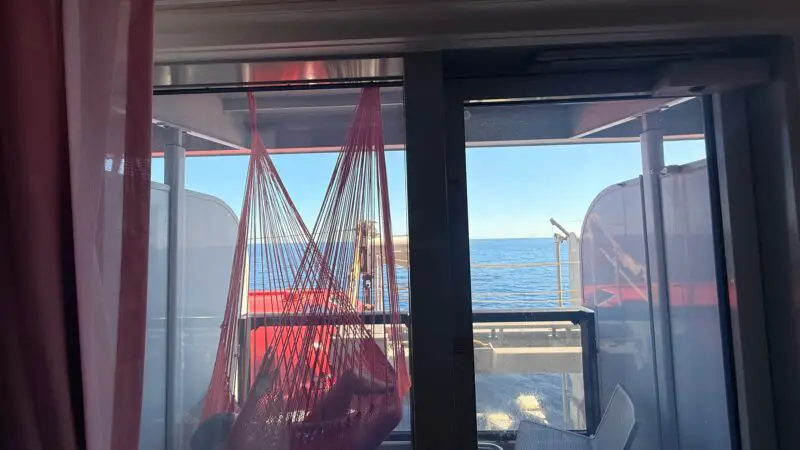 Virgin Voyages cruise ship cabin with a balcony featuring a red hammock and ocean view.